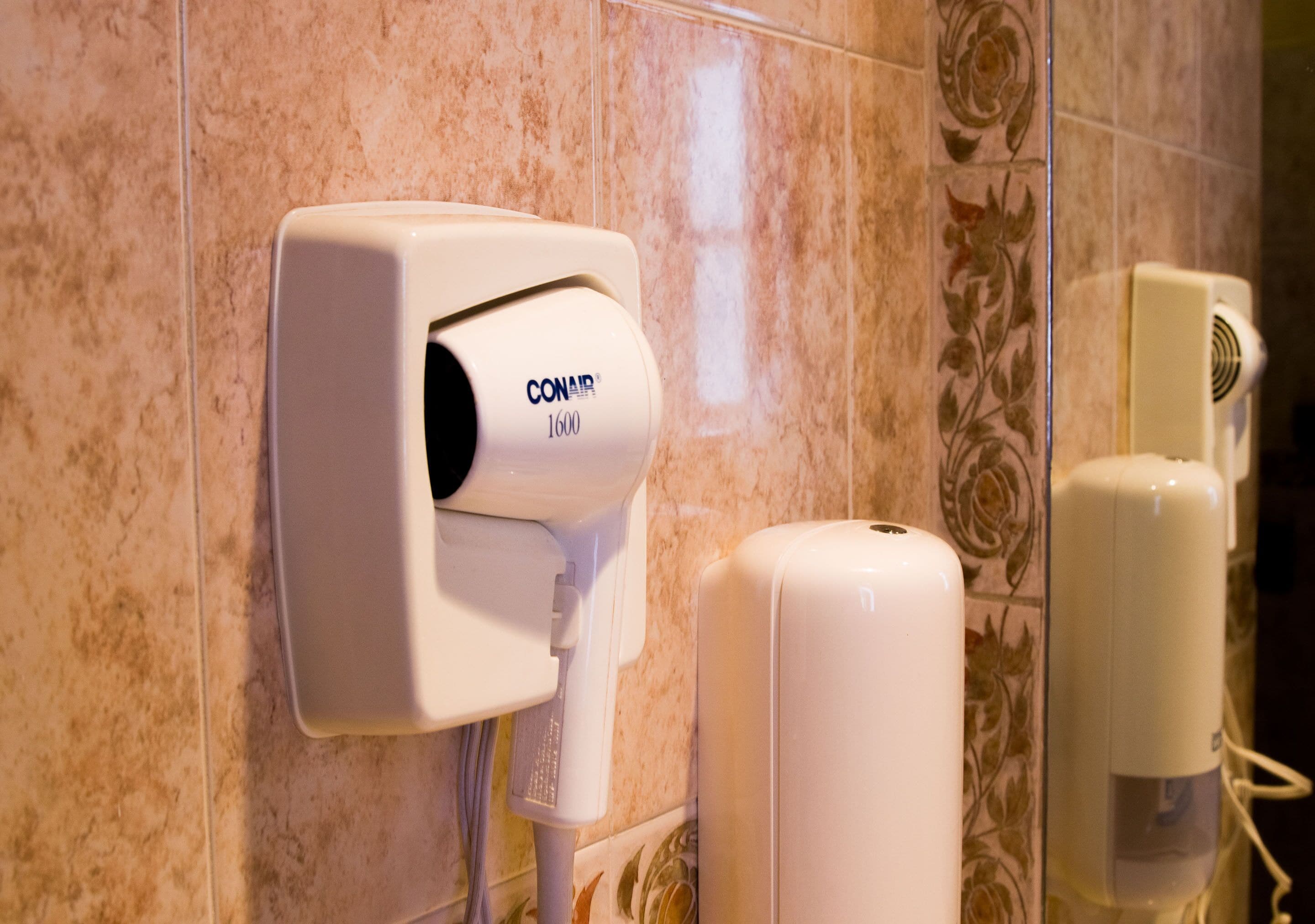 A hand dryer and a paper towel dispenser mounted on a tiled wall.