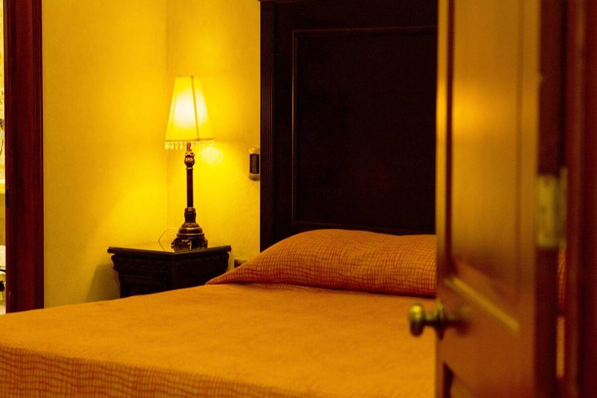 A hotel room with a bed, a nightstand, a lamp, and a door.