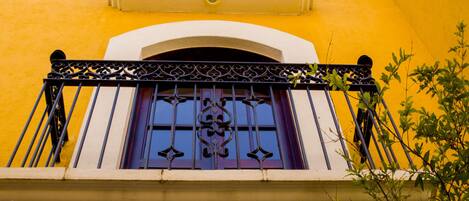 A yellow building with a balcony featuring ornate metal railings and a purple window.