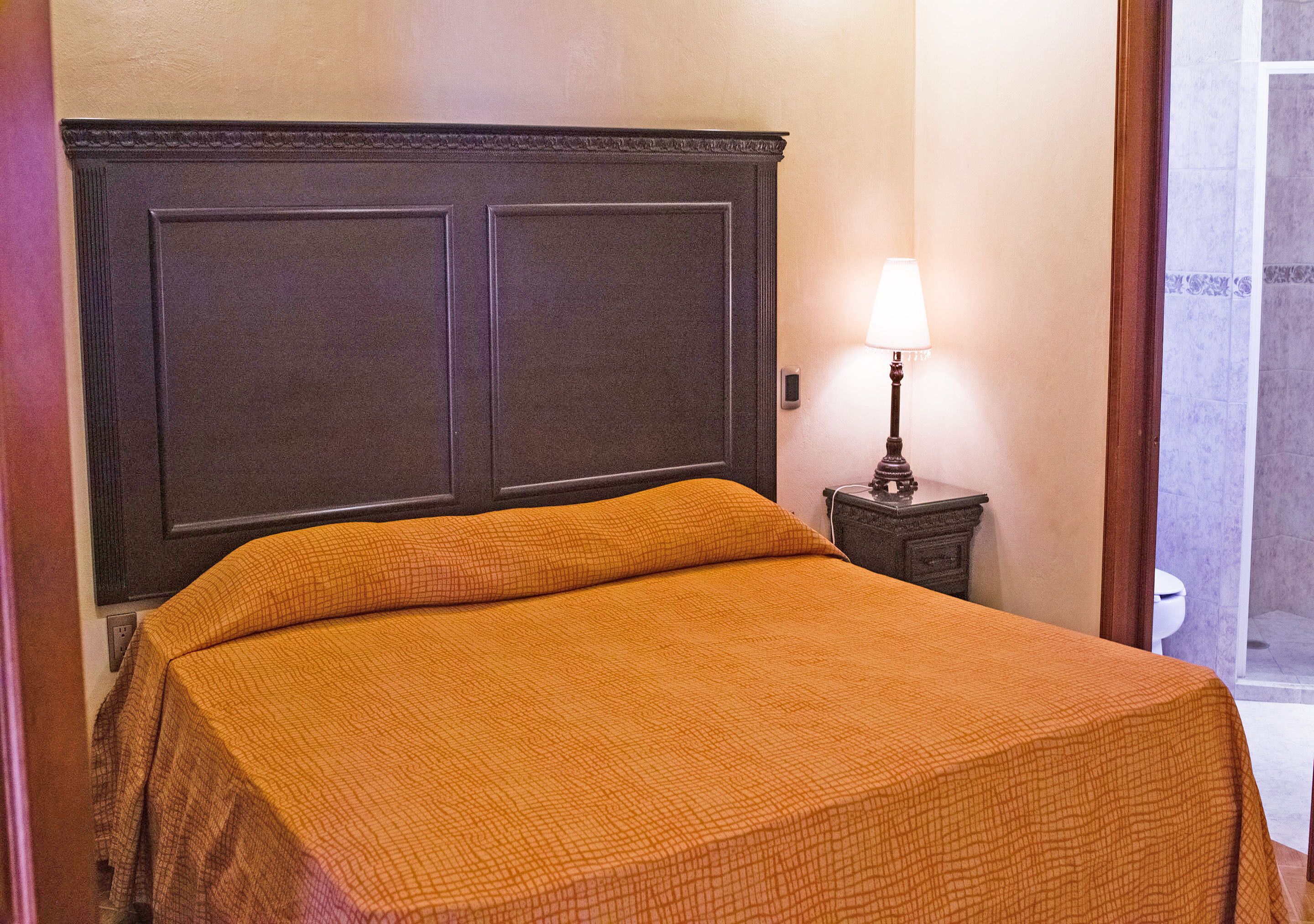 A room with a bed, a nightstand with a lamp, and a door.