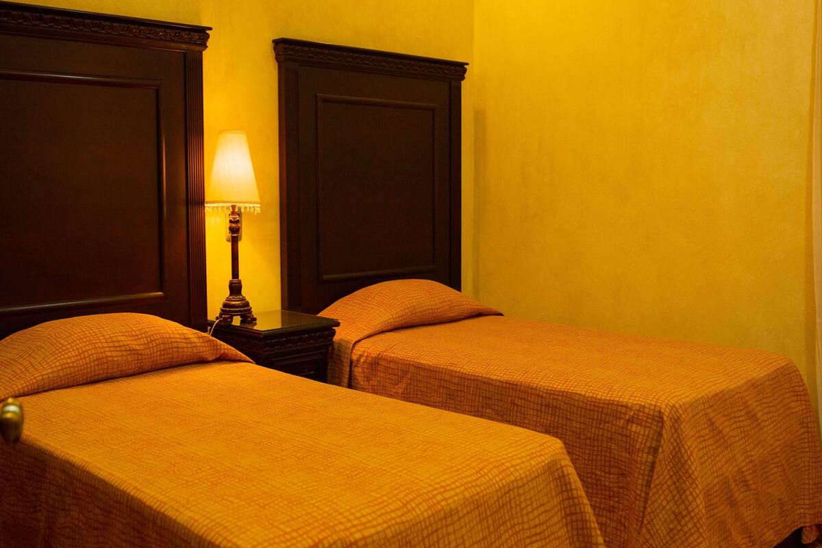 A hotel room with two beds, a nightstand with a lamp, and a wooden headboard.