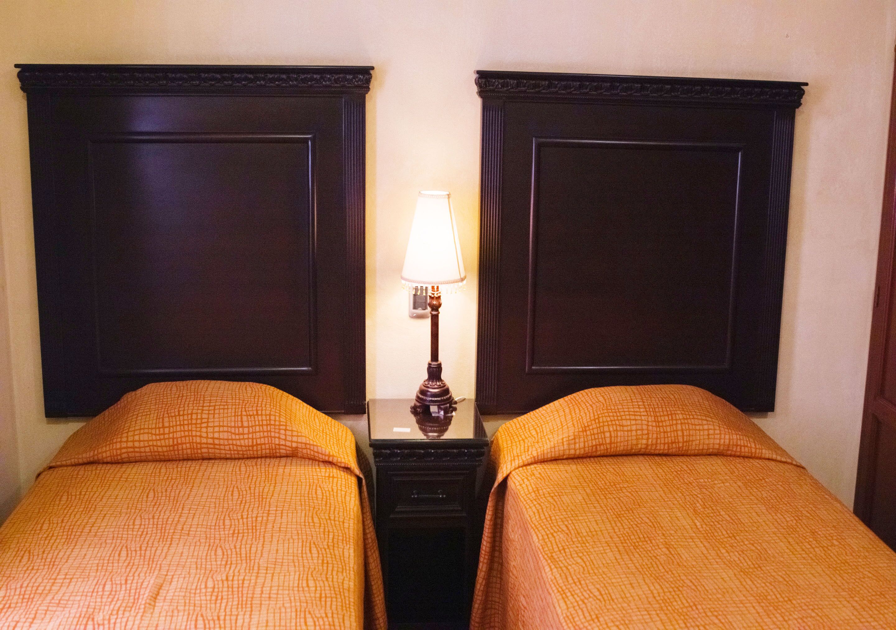 Ein Hotelzimmer mit zwei Betten, jeweils mit einer orangefarbenen Tagesdecke, einem Nachttisch mit Lampe und dunklen Holz-Kopfteilen.