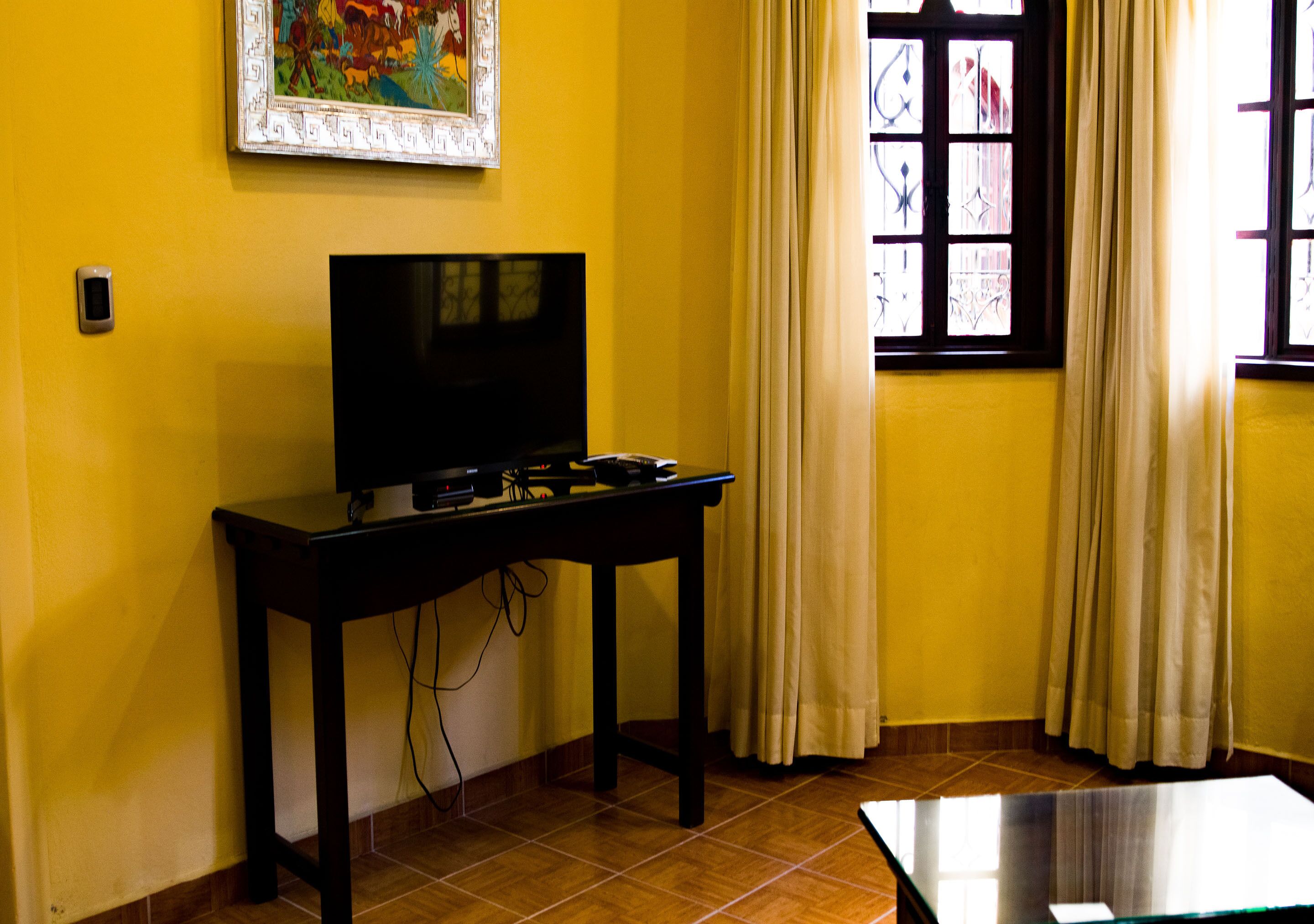 A room with a television on a table, a window with curtains, and a tiled floor.