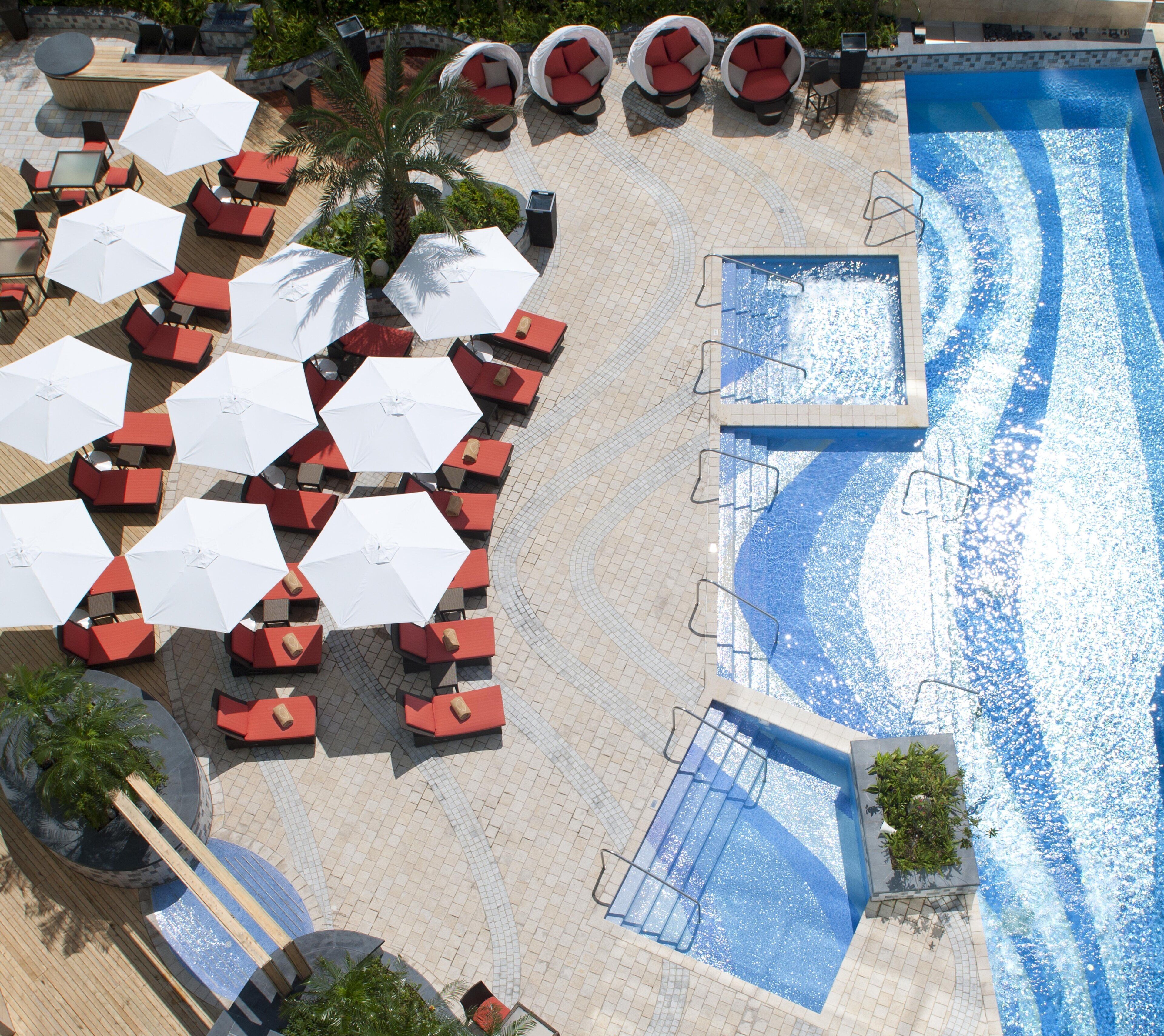 An aerial view of a resort with a swimming pool, sun loungers, and umbrellas.
