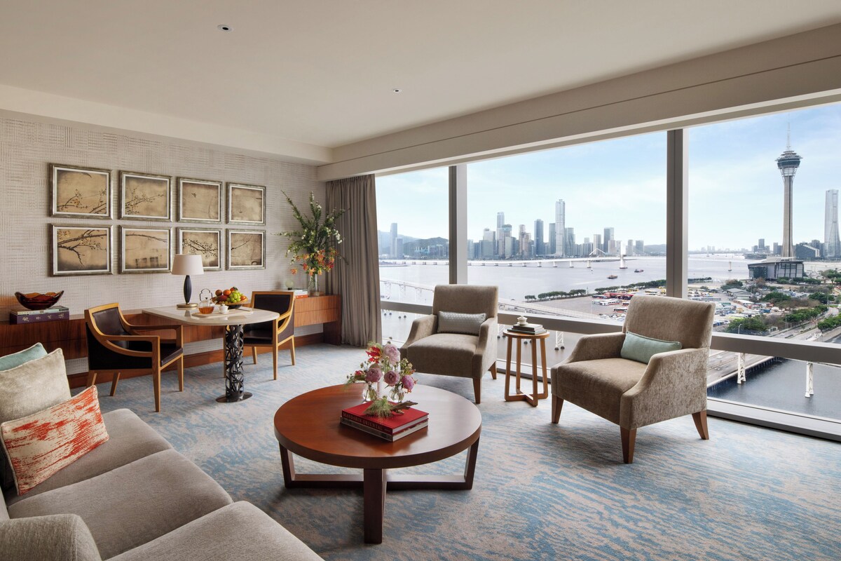 A modern hotel room with a large window offering a city skyline and water view.