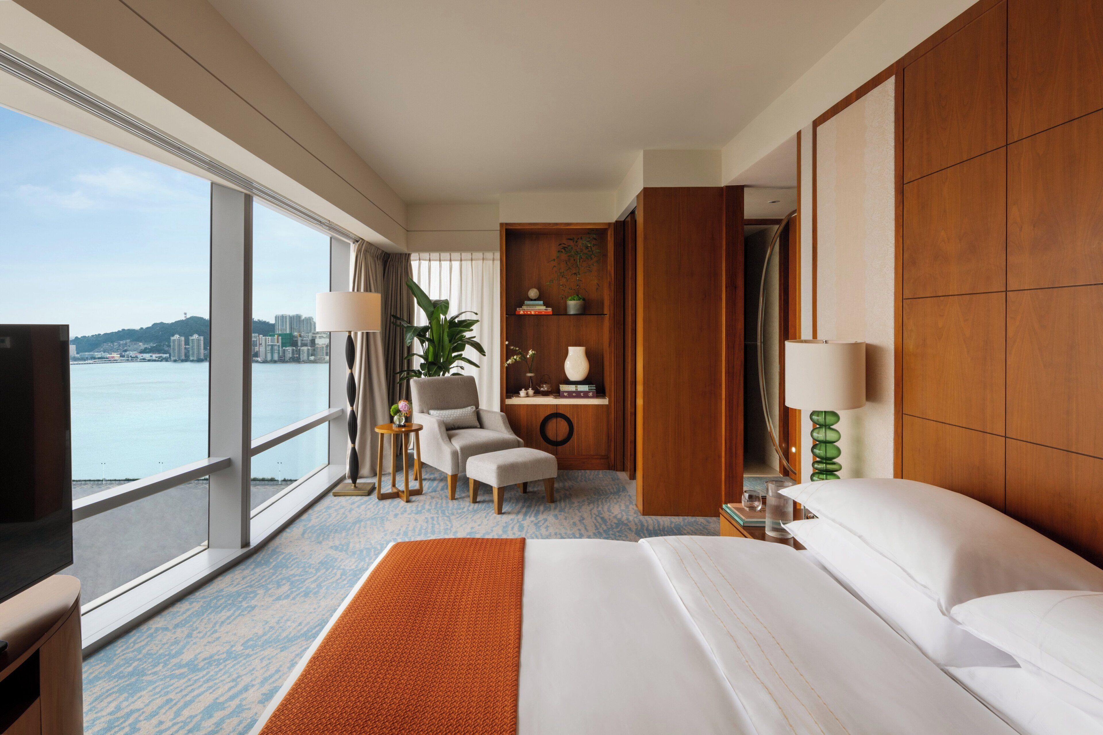 A hotel room with a large bed, a desk with a chair, a view of the city, and a window with curtains.