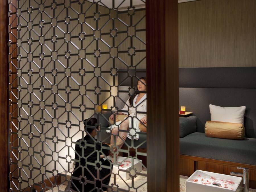 Et værelse med en geometrisk afskærmning, en sofa med puder, et sengebord med en lampe og et lille sengebord med en blomstervase.