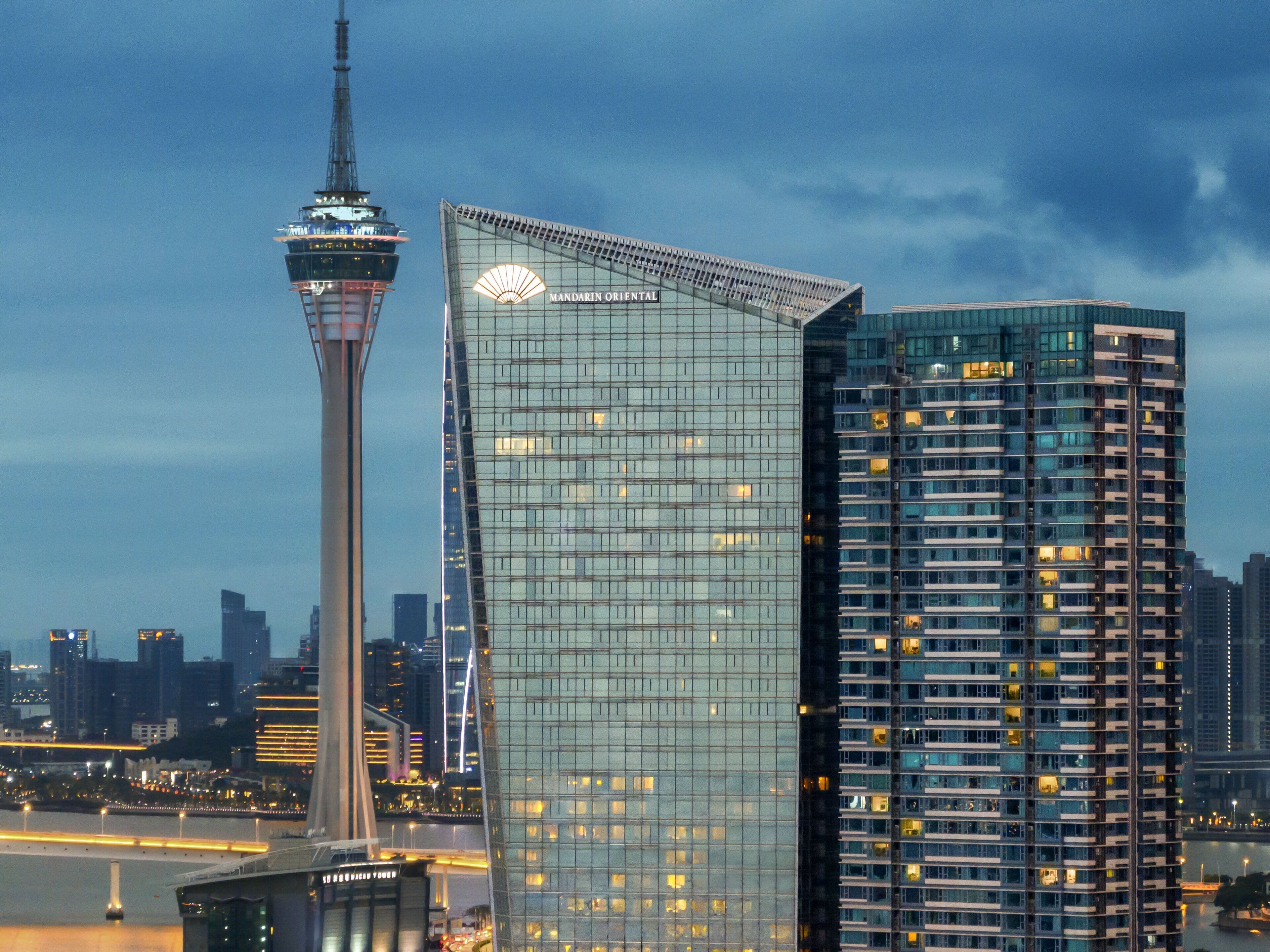 Un moderno edificio de gran altura con fachada de vidrio y una estructura de torre distintiva al fondo.