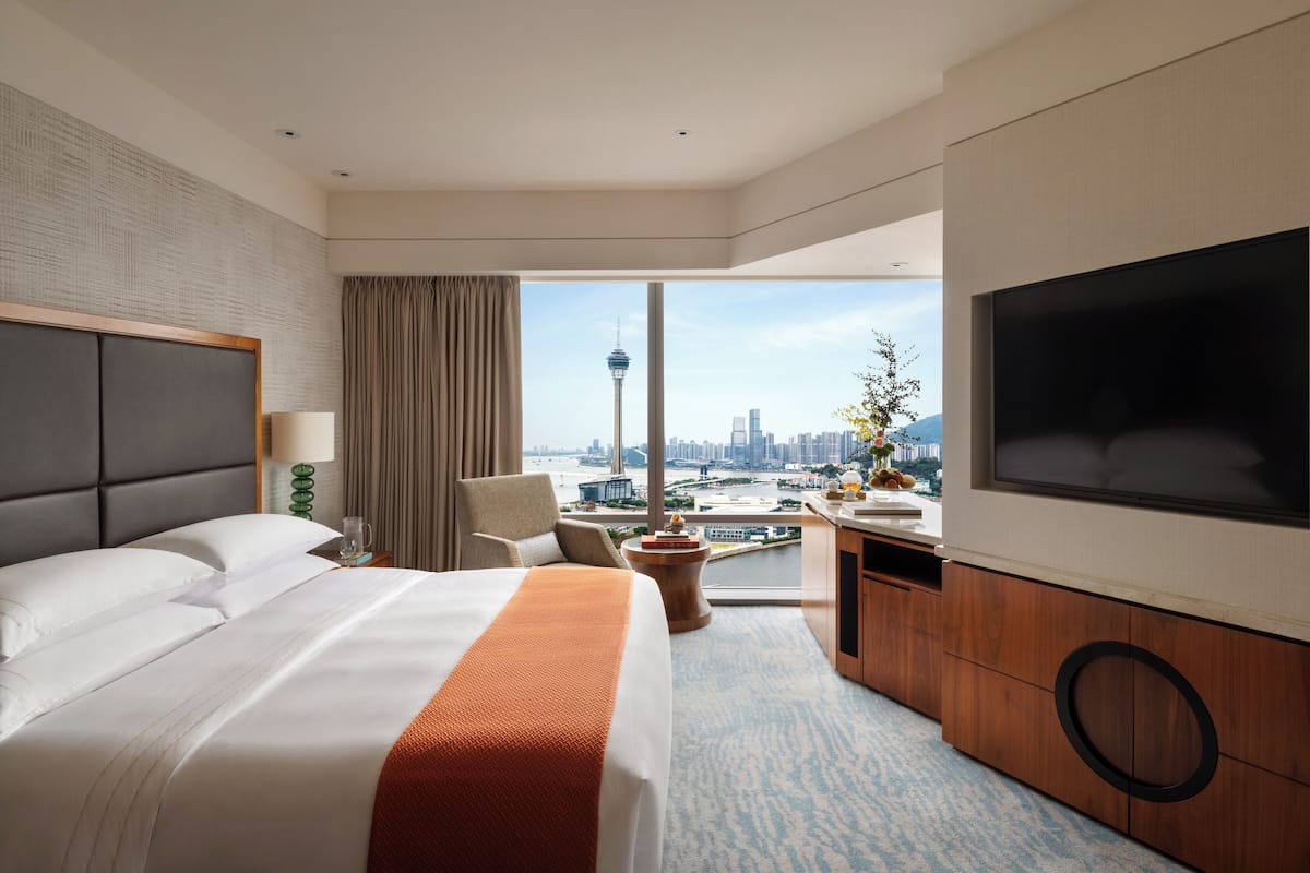 A hotel room with a large bed, a TV, a desk, and a view of a cityscape.