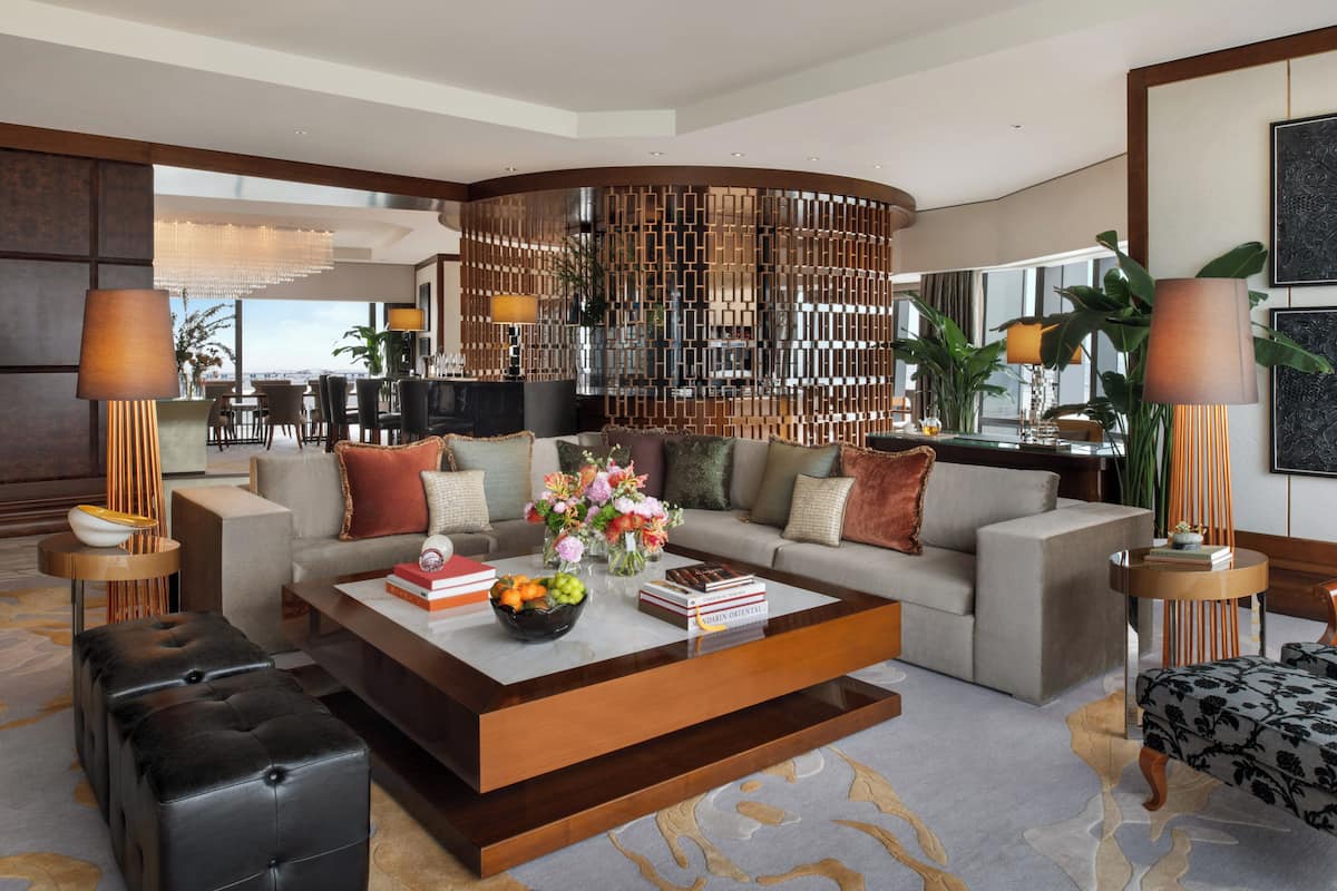 A modern living room with a large sectional sofa, a coffee table with books and fruit, and a decorative wall panel.