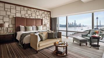 Habitación de hotel con una cama grande, un sofá, una mesita y vistas a un horizonte urbano.