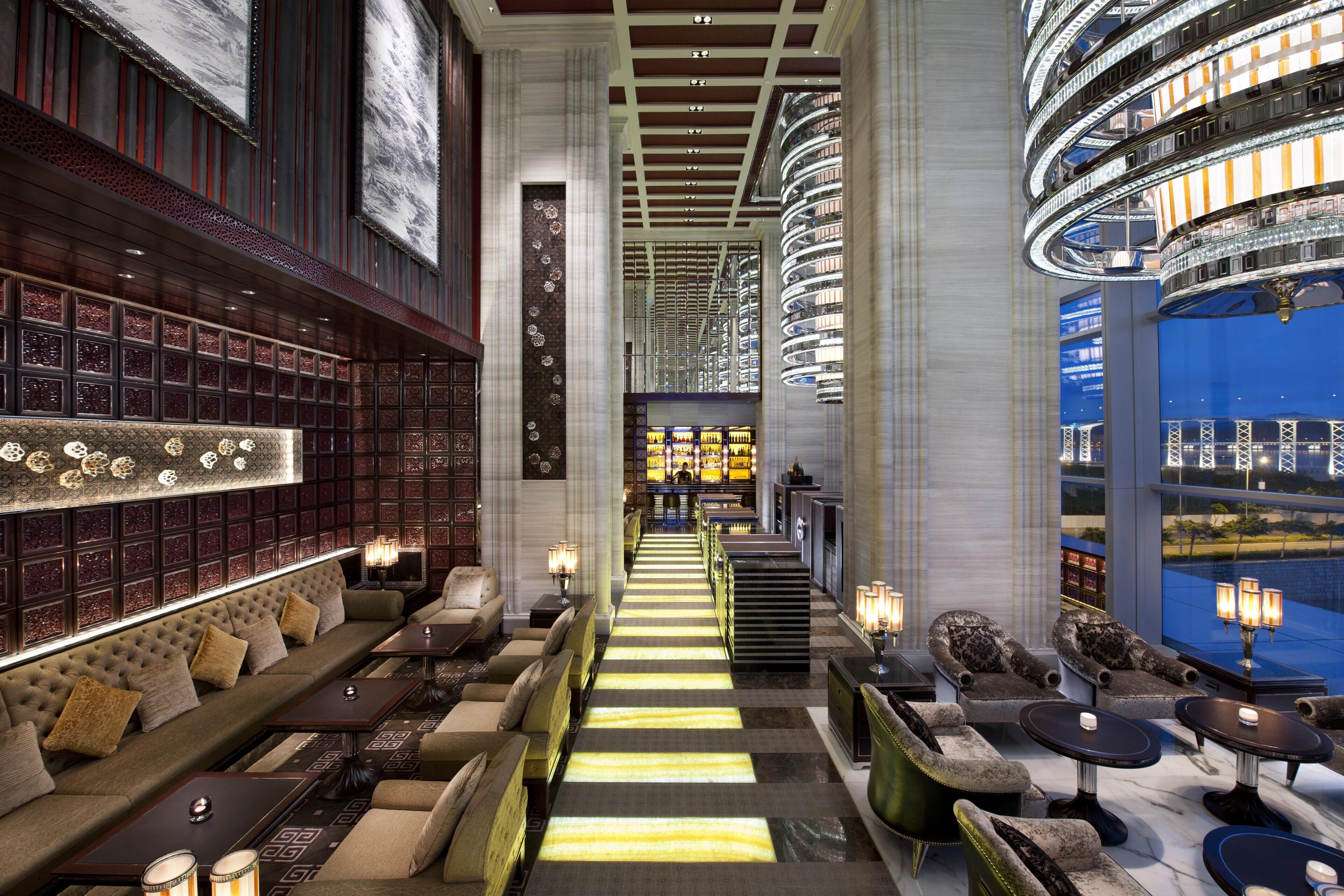 Um hall de hotel com uma escadaria central, áreas de estar e um bar.