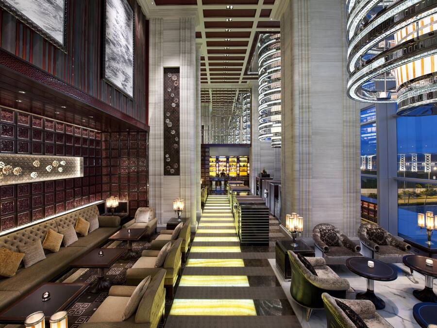 Um hall de hotel com uma escadaria central, áreas de estar e um bar.