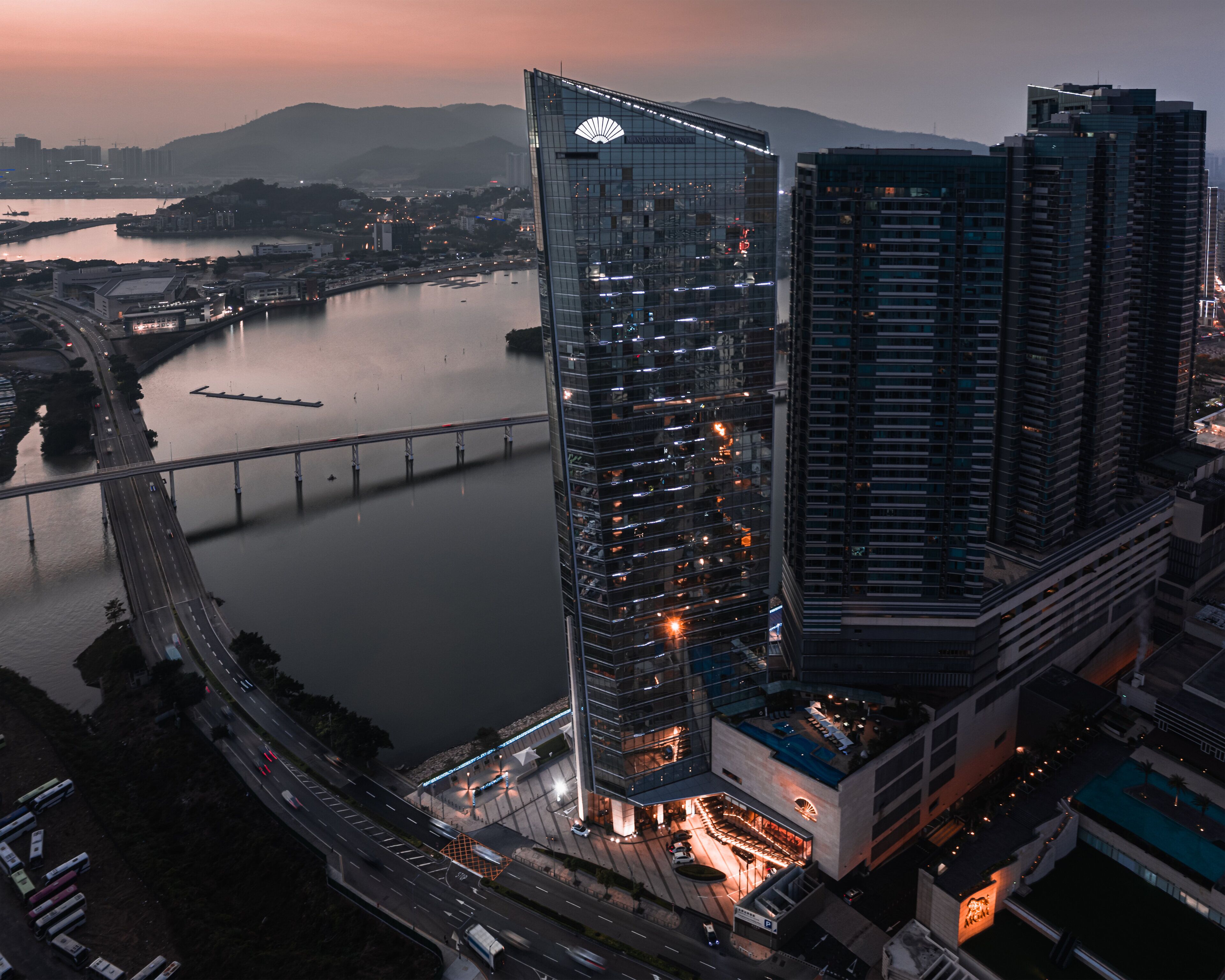 A high-rise building with a glass facade, a bridge in the background, and a waterfront.