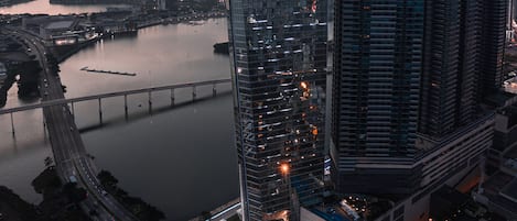 Un edificio moderno de gran altura con fachada de vidrio, un puente al fondo y una vista al agua.