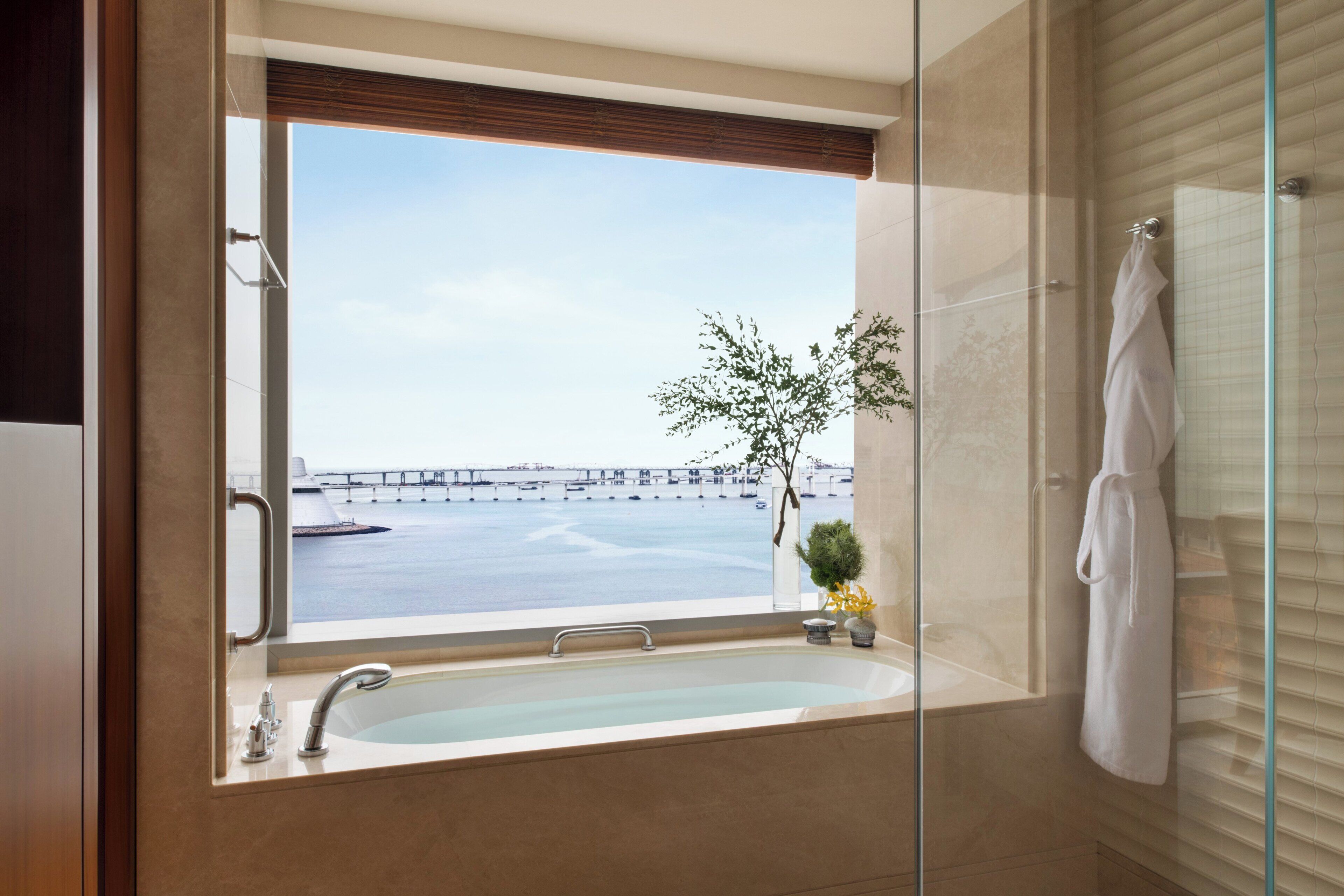 A modern bathroom with a large window, a bathtub, and a glass shower enclosure.
