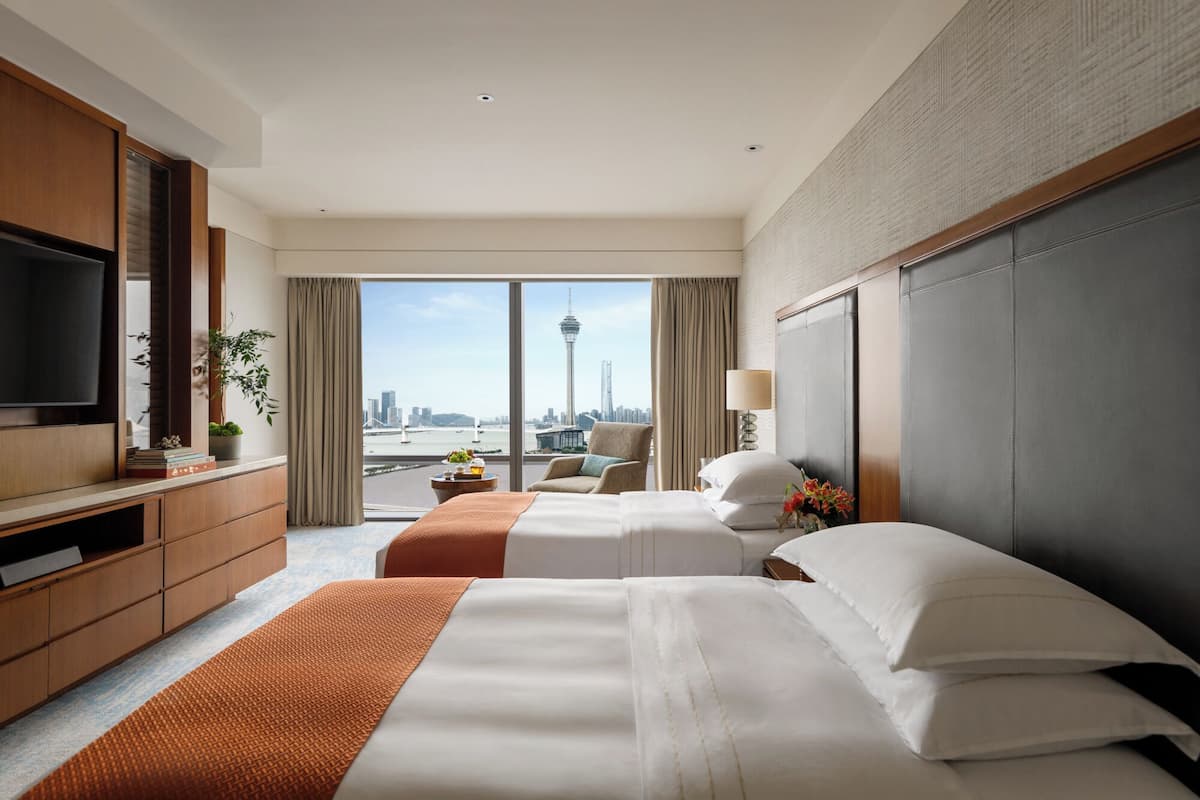 A hotel room with a large bed, a TV, a desk, and a view of a cityscape.