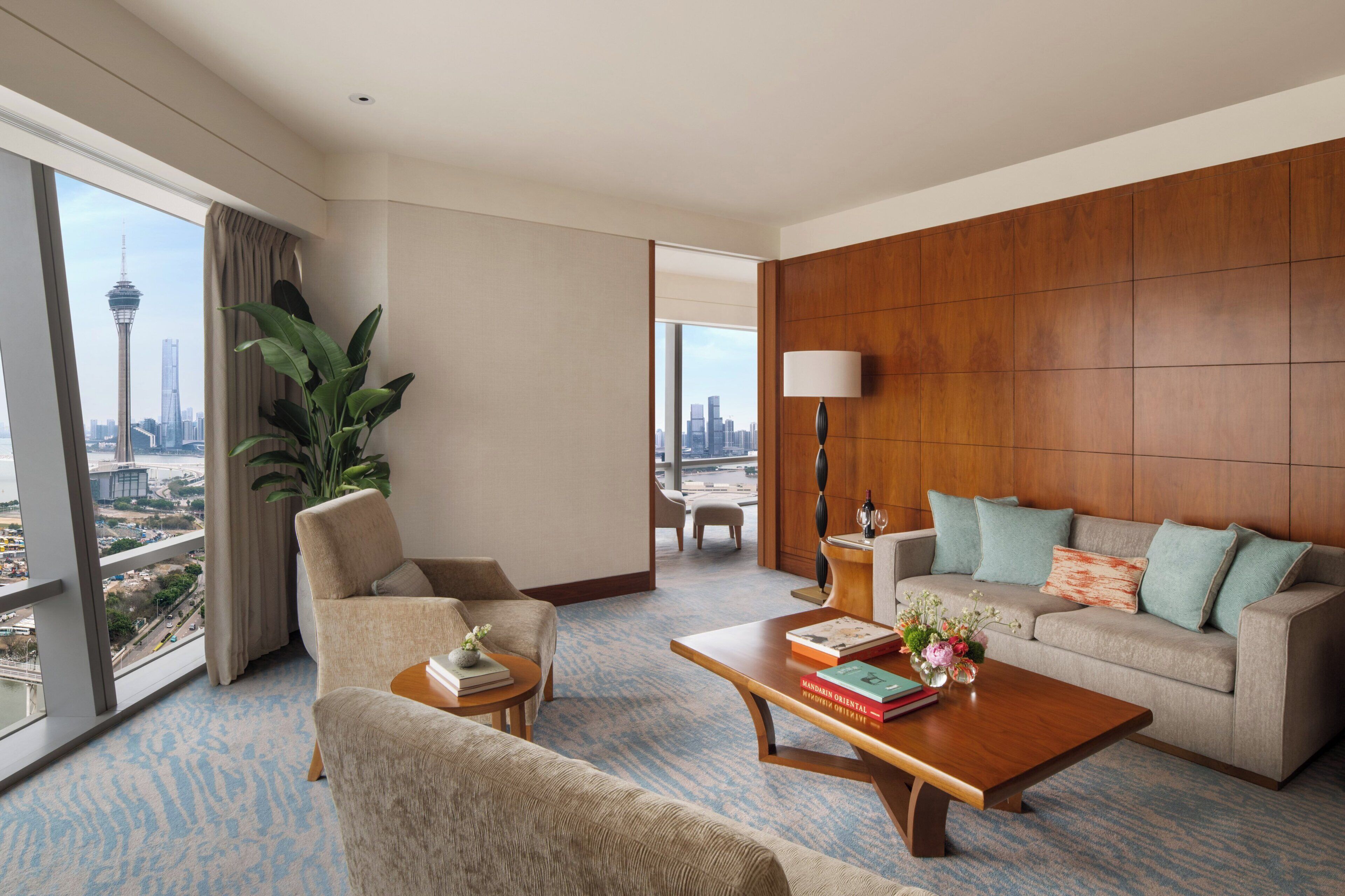Habitación de hotel con un ventanal grande, un sofá, una mesa de centro y una planta en maceta.