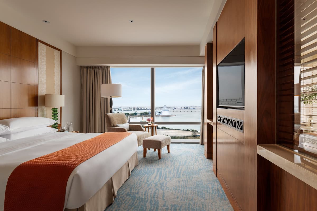 A hotel room with a large bed, a TV, a small table, and a view of a bridge.