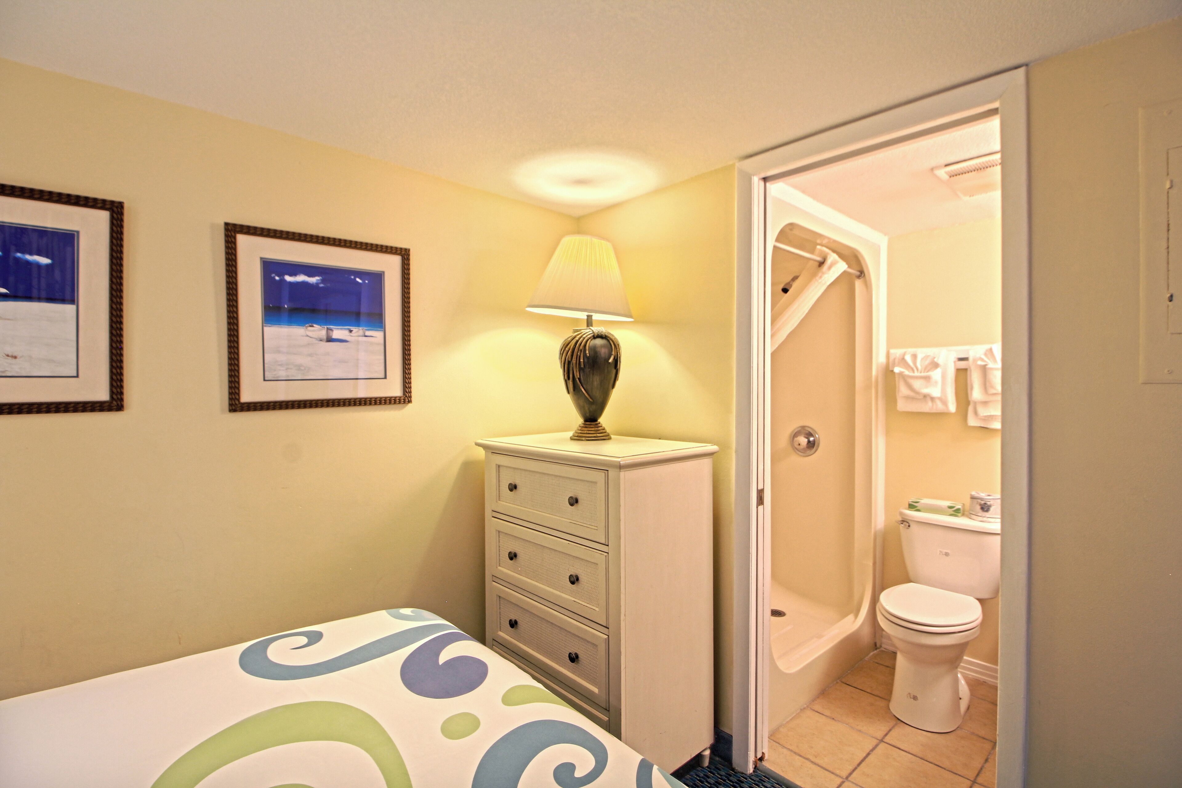 Une chambre à coucher avec un lit, une commode, une lampe et deux tableaux encadrés accrochés au mur.