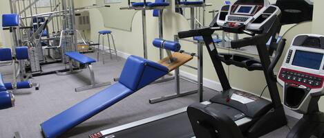 Un gimnasio con equipo de ejercicio, incluyendo cintas de correr, máquinas de pesas y bancos.