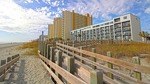 A beachfront hotel with multiple high-rise buildings, a wooden boardwalk, and beach vegetation.
