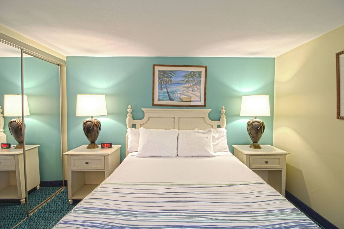 A hotel room with a bed, two bedside tables, two lamps, a painting, and a mirror.