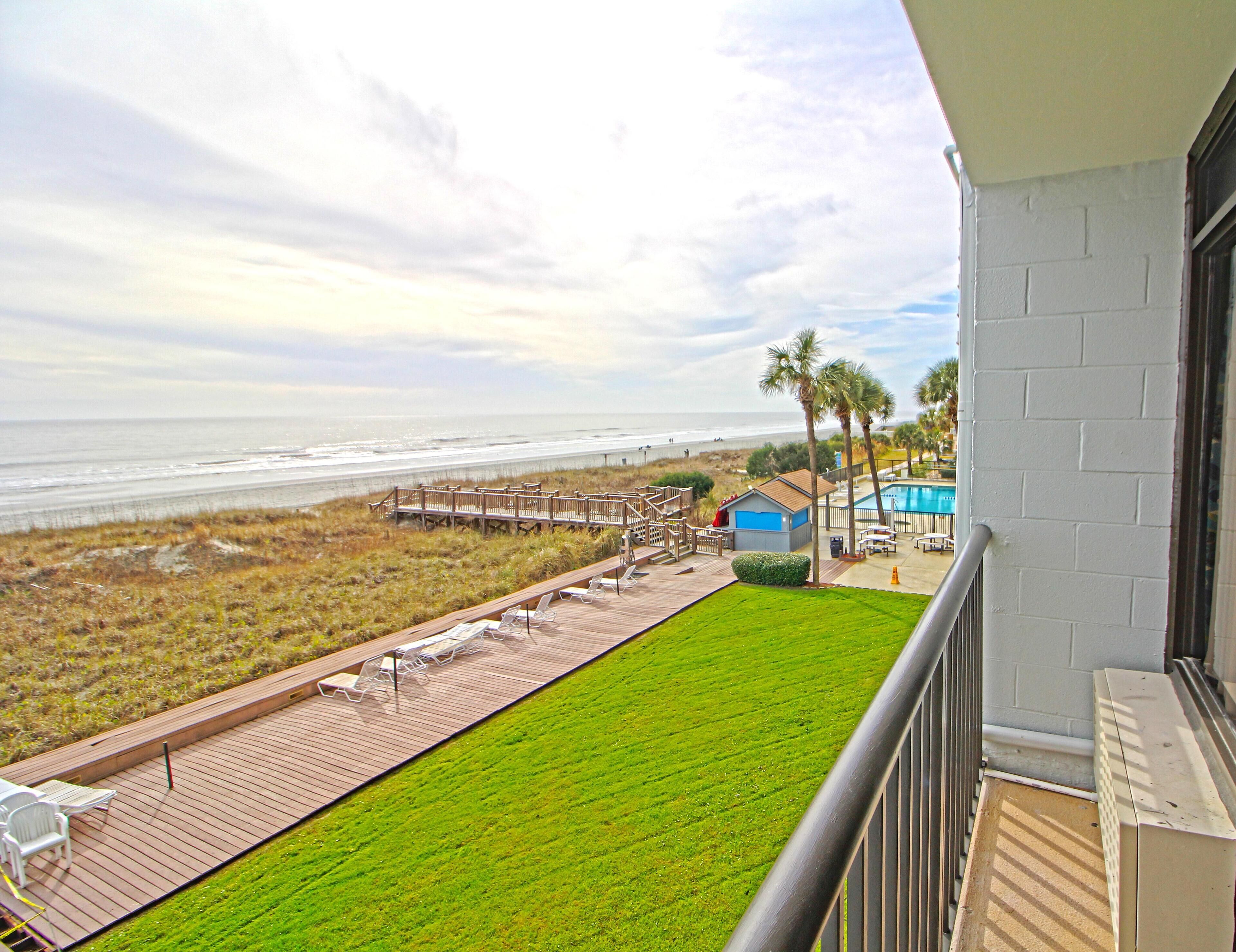 Ein Balkon mit Blick auf den Strand, einen Pool und ein kleines Gebäude.