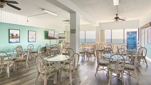 A dining area with wicker chairs and tables, a ceiling fan, and a view of the ocean.