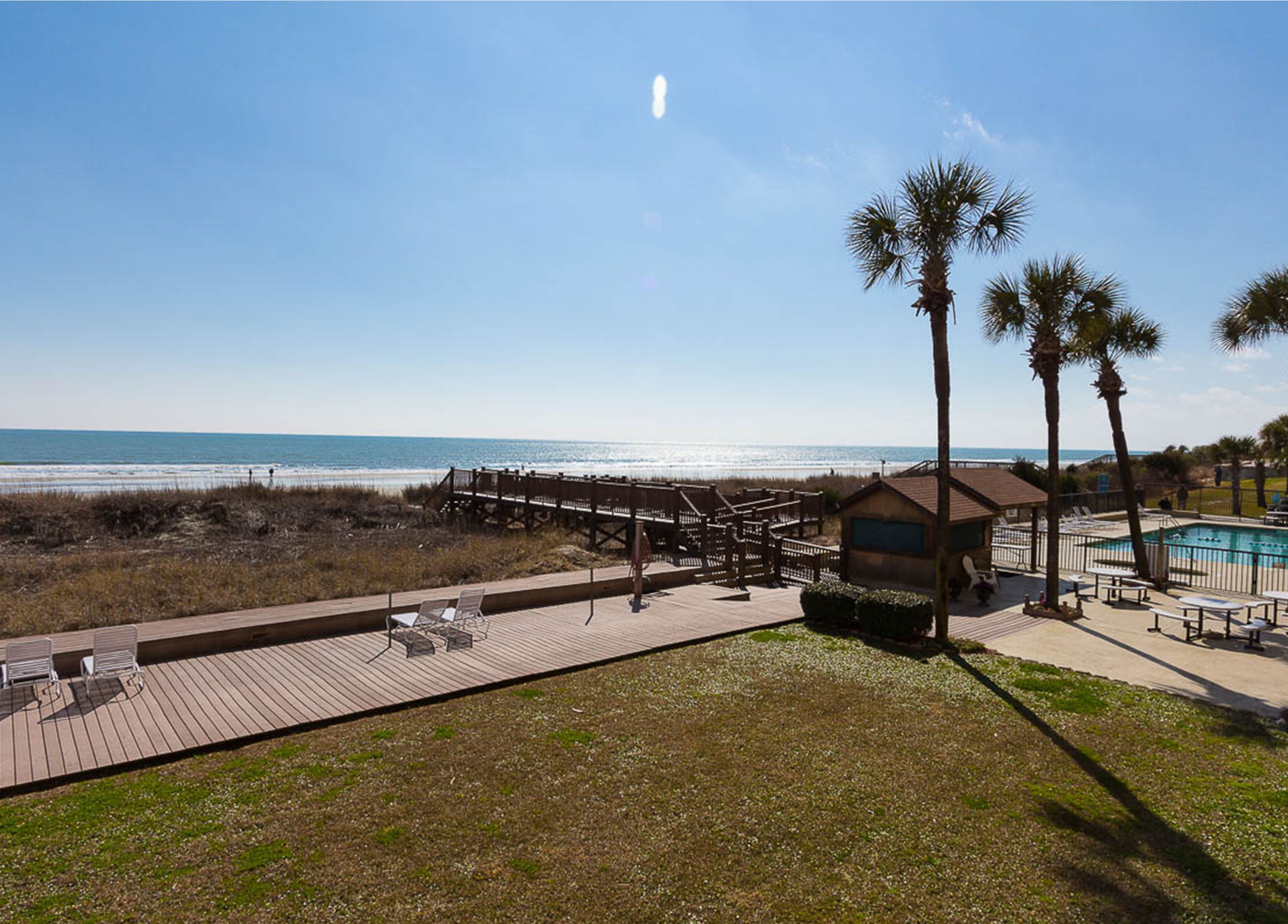 A beachside resort with a wooden deck, a pool, and a view of the ocean.