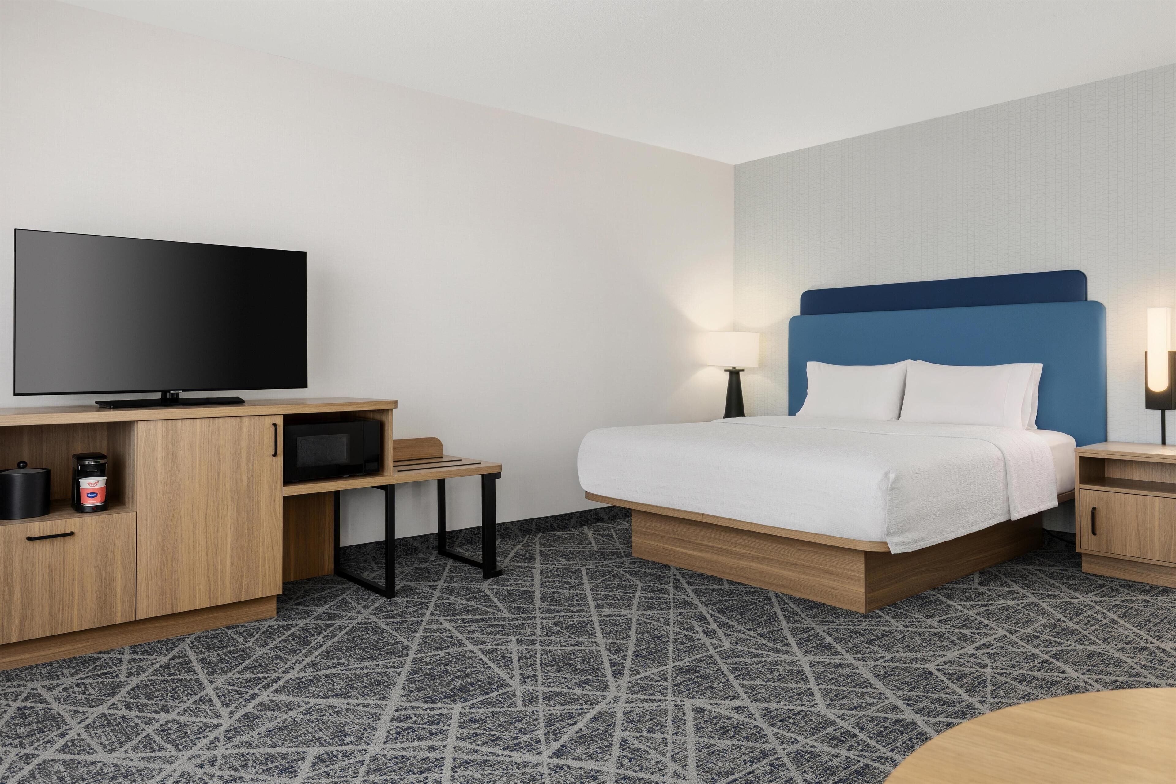 A hotel room with a bed, a television, a desk with a computer, a microwave, and a coffee maker.