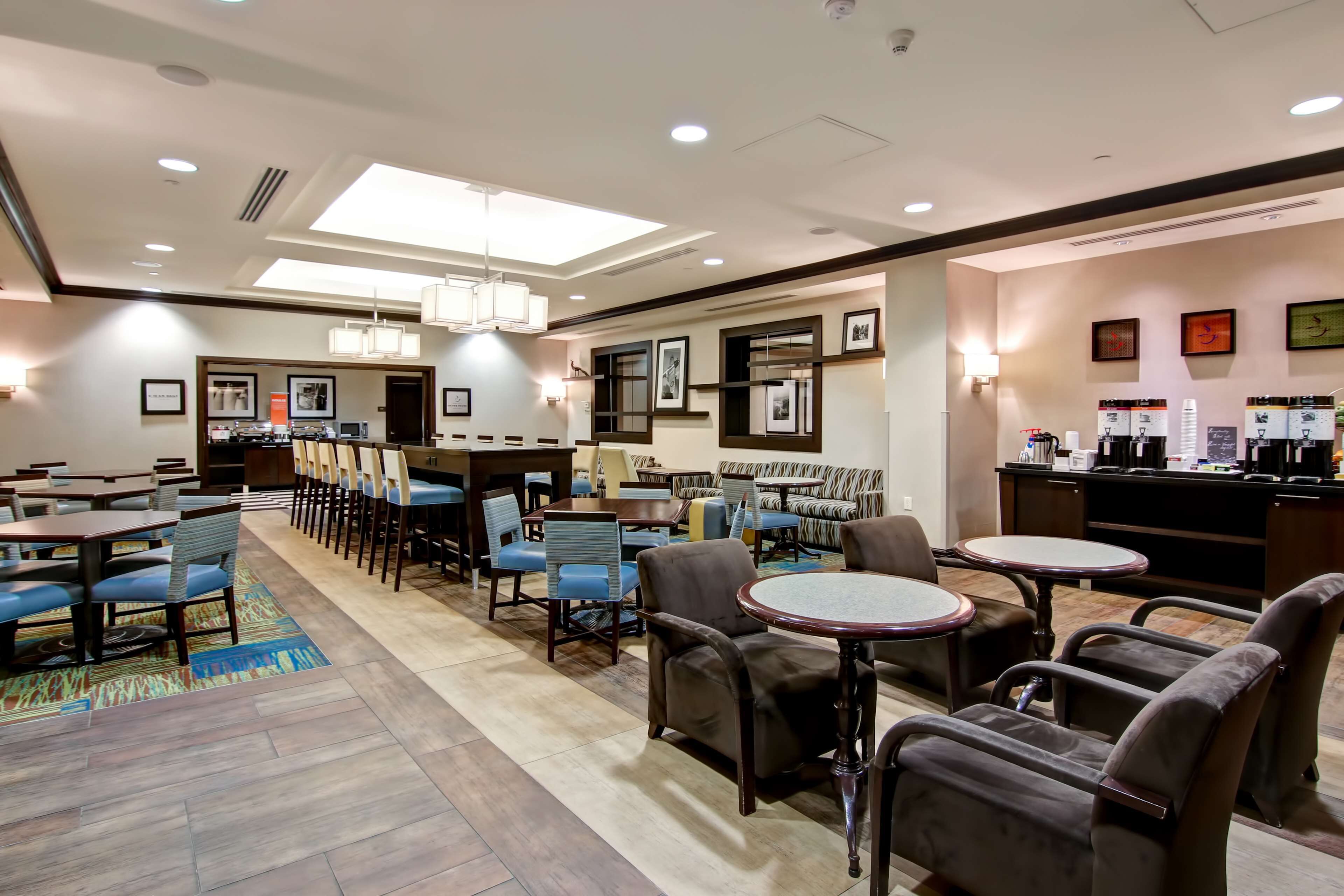 Un hall de hotel con varias zonas de estar, incluyendo mesas y sillas, un mostrador de recepción y cuadros en las paredes.