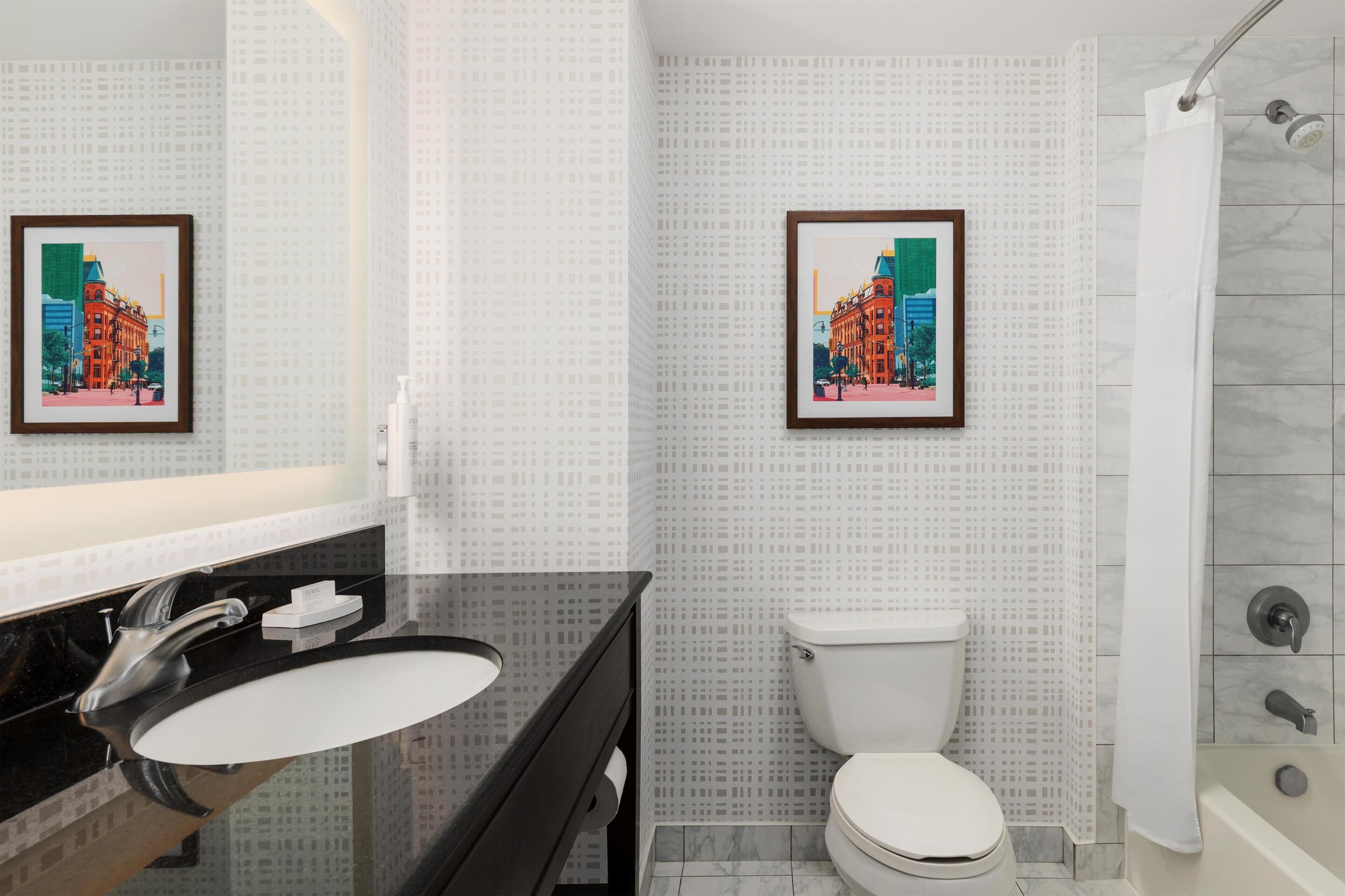 A bathroom with a black sink, white toilet, and a shower with a glass door. There are two framed pictures on the wall.
