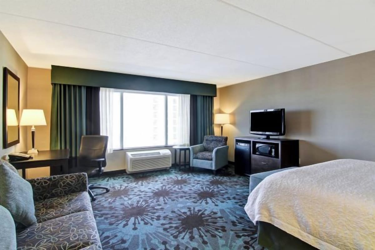 Une chambre d’hôtel comprenant un lit, un canapé, une chaise, une télévision, un bureau et une fenêtre avec des rideaux.