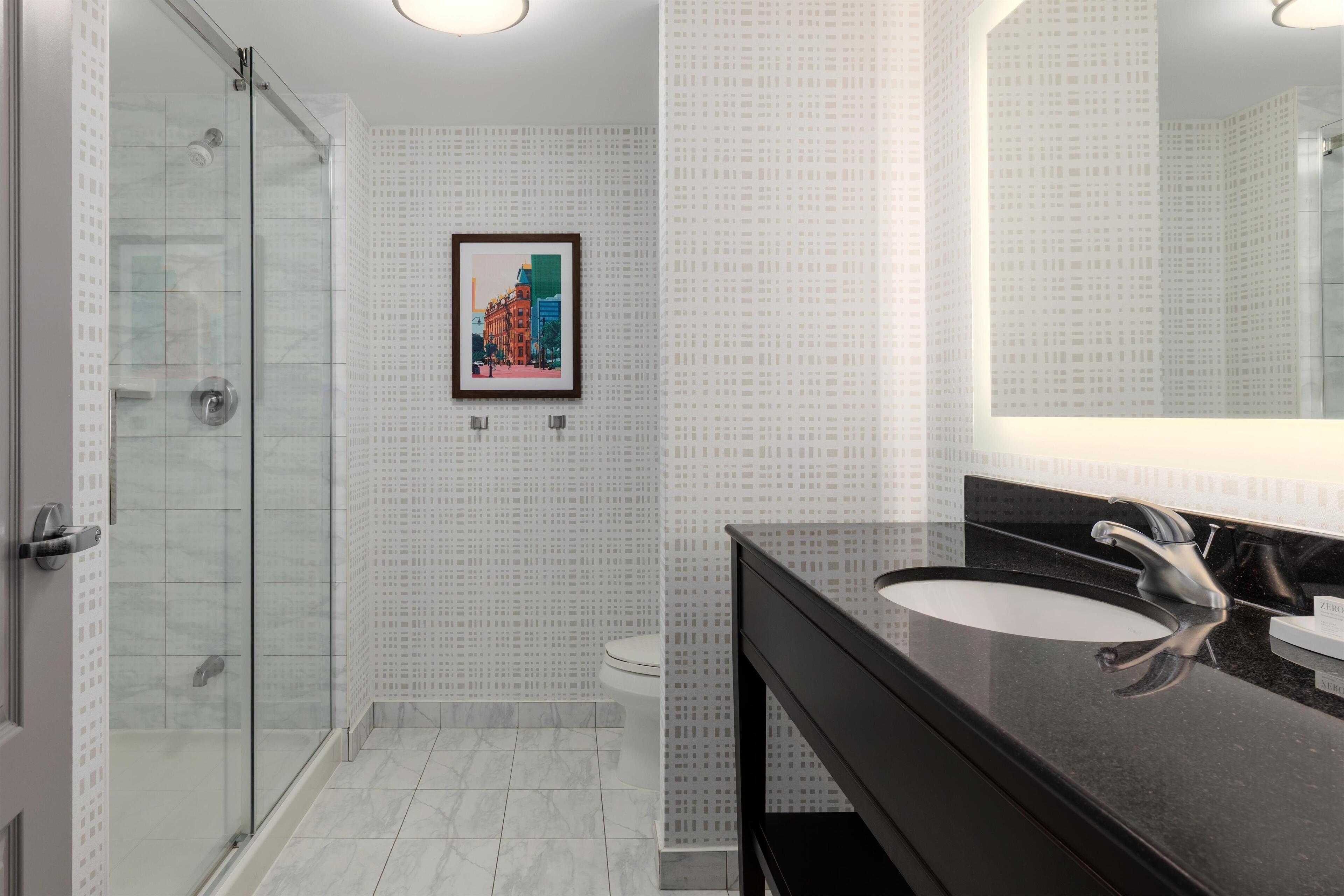 A modern bathroom with a glass shower enclosure, a large mirror, and a black countertop with a sink.