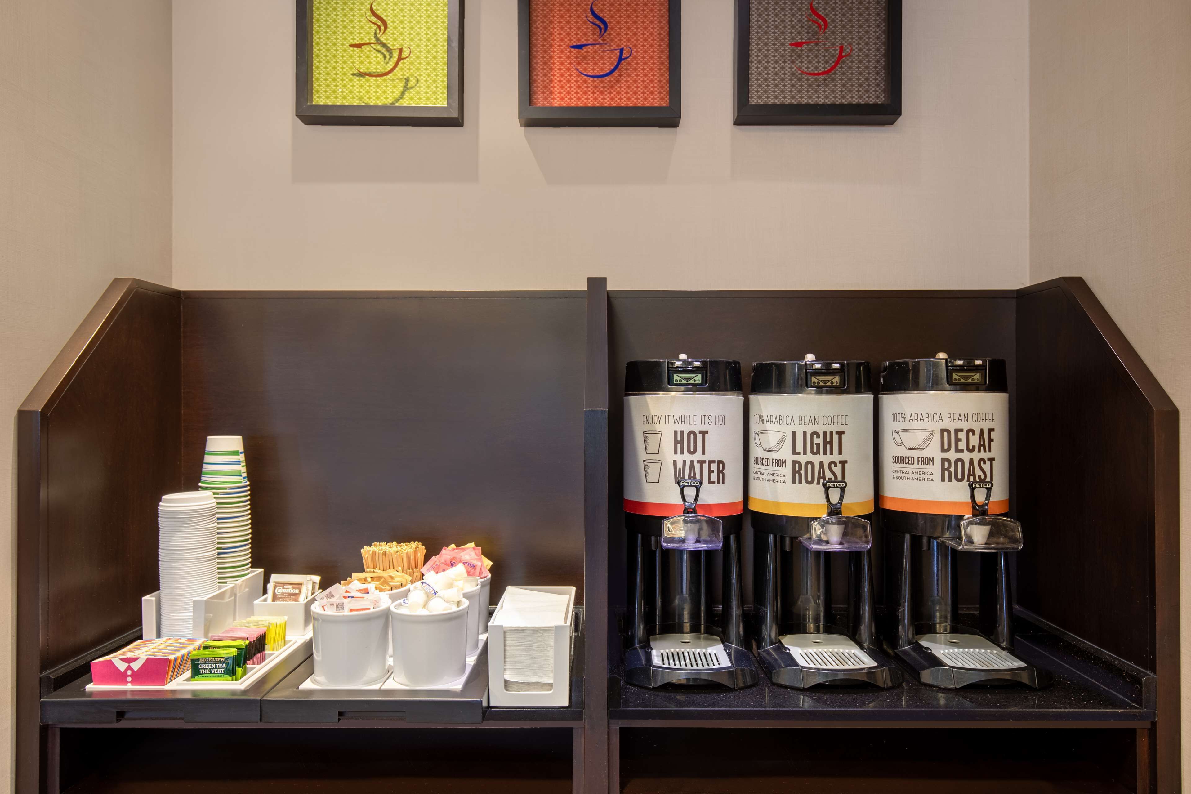 A breakfast bar with coffee dispensers, plates, and food items.