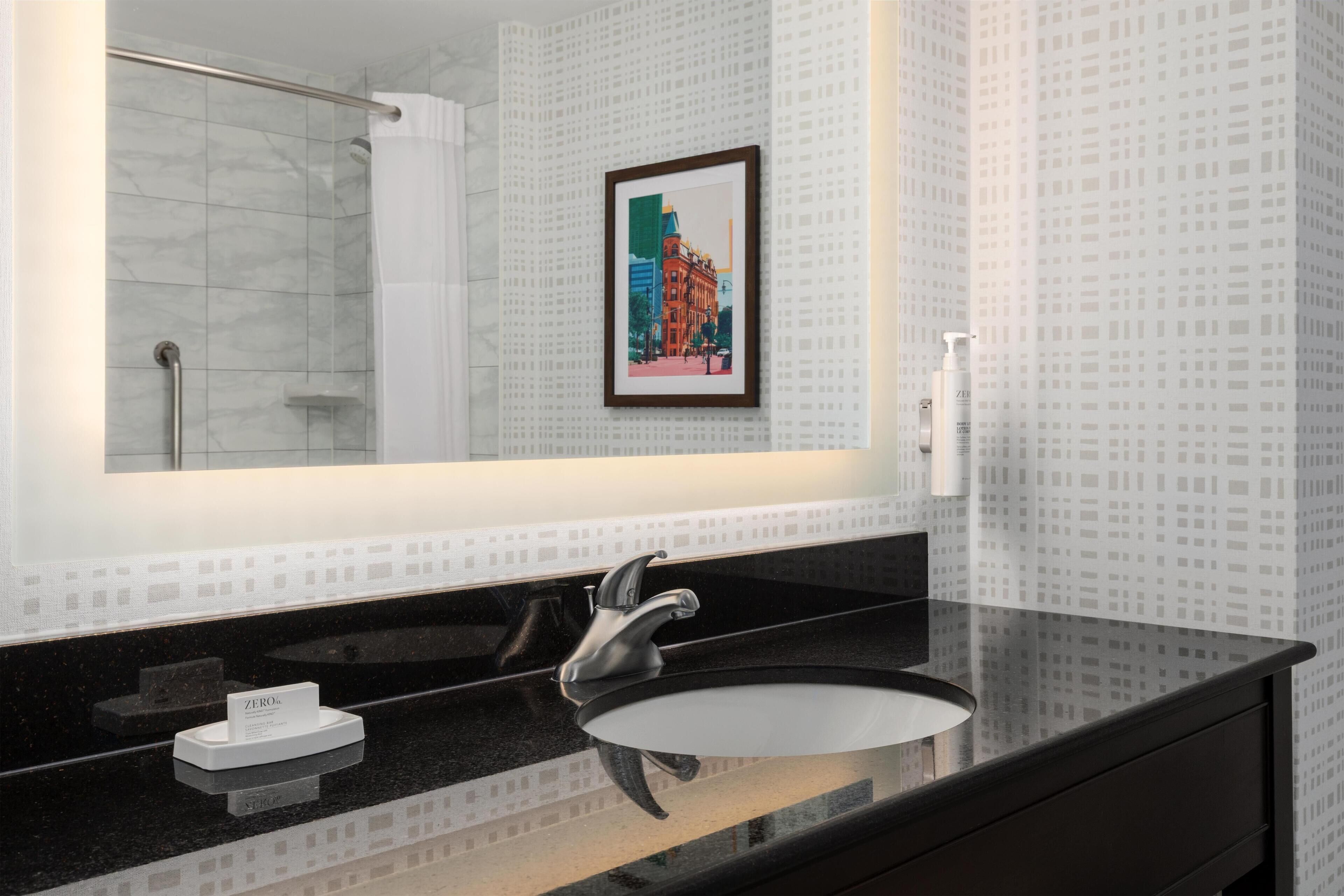 Ein Badezimmer mit schwarzem Waschtisch, einer weißen Spüle, einem gerahmten Bild an der Wand und einer Duschkabine.