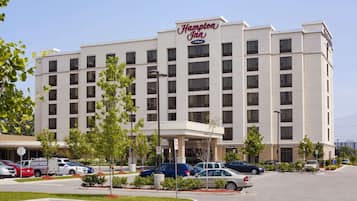A Hampton Inn hotel with a modern design, featuring a prominent entrance and a parking lot with several cars.