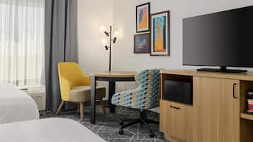 Habitación de hotel con cama, escritorio con computadora, silla, televisor y obras de arte en la pared.