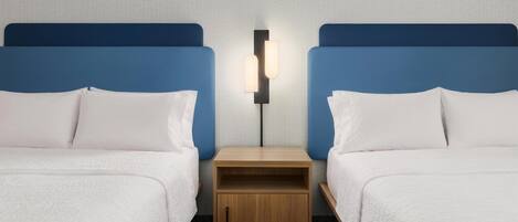 A hotel room with two beds, a nightstand, and a wall-mounted light fixture.