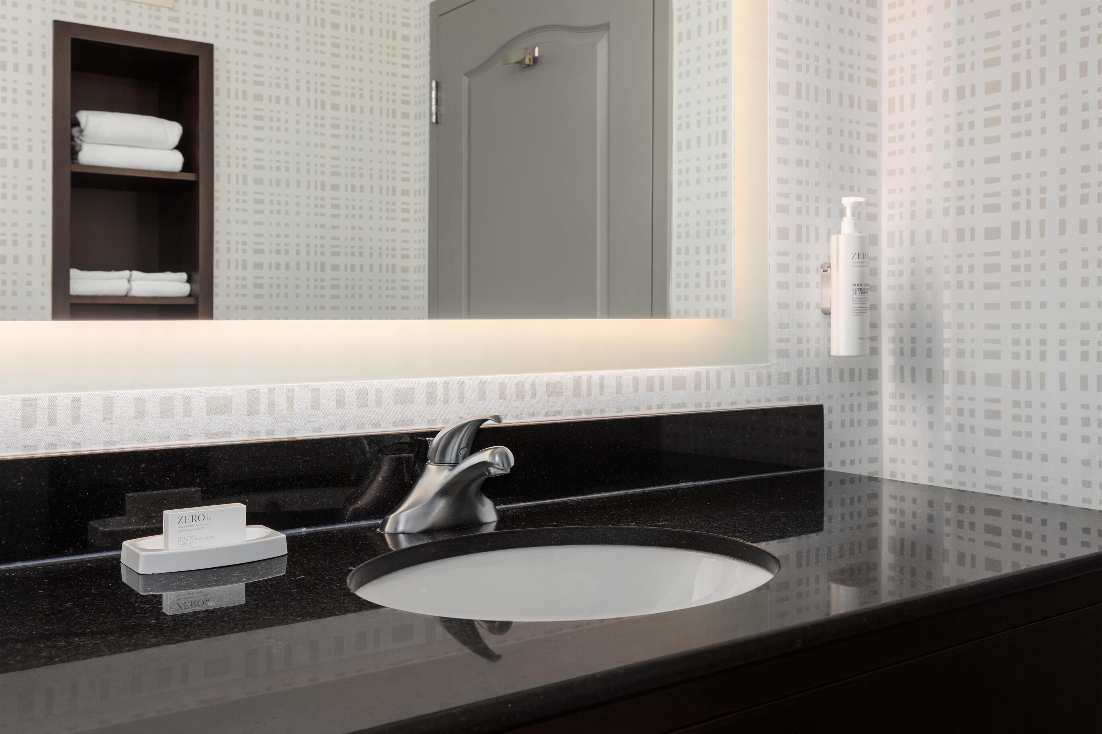 A bathroom with a black countertop, a single sink, a mirror above the sink, and a towel rack with folded towels.