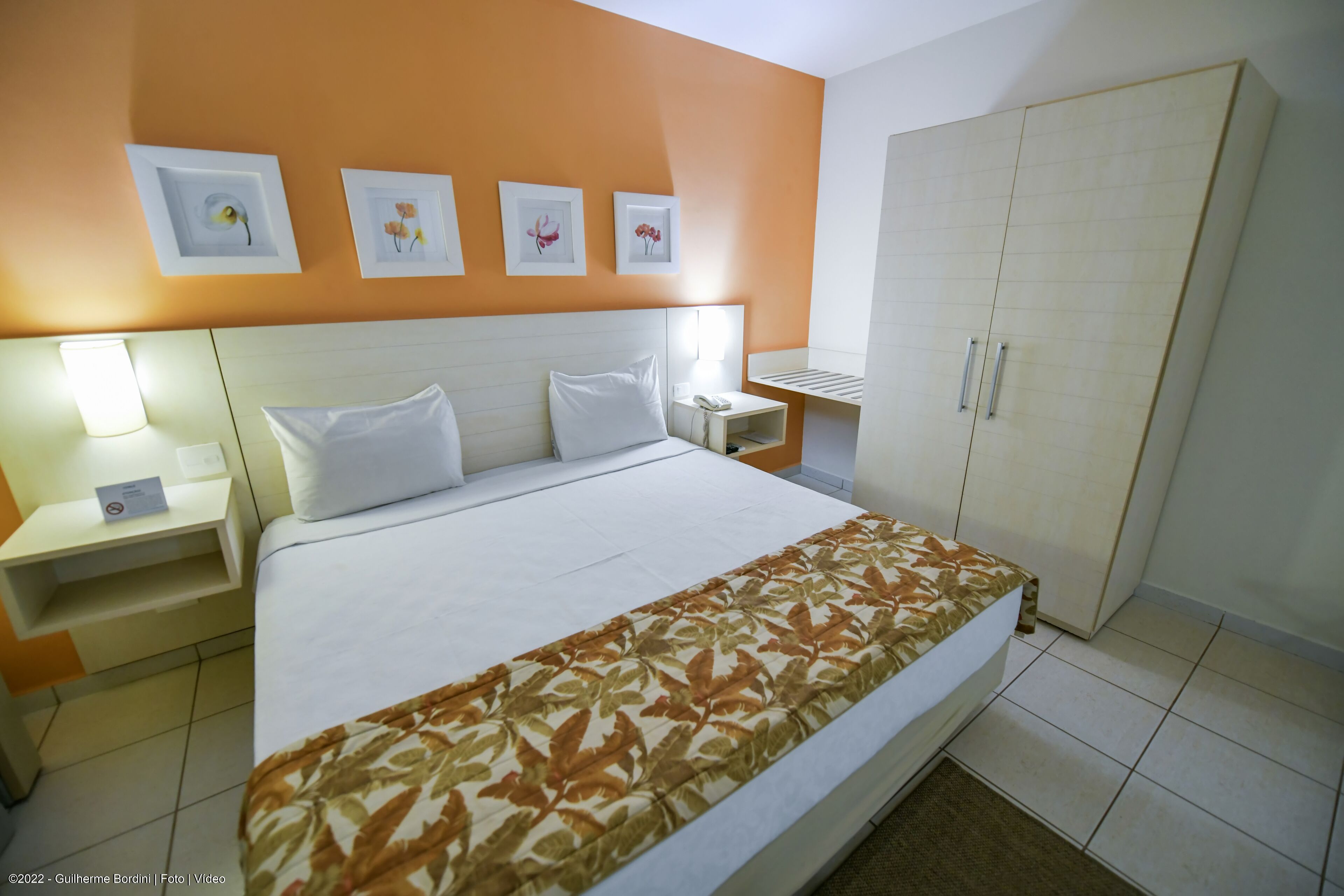 A hotel room with a bed, nightstands, a wardrobe, and wall-mounted artwork.
