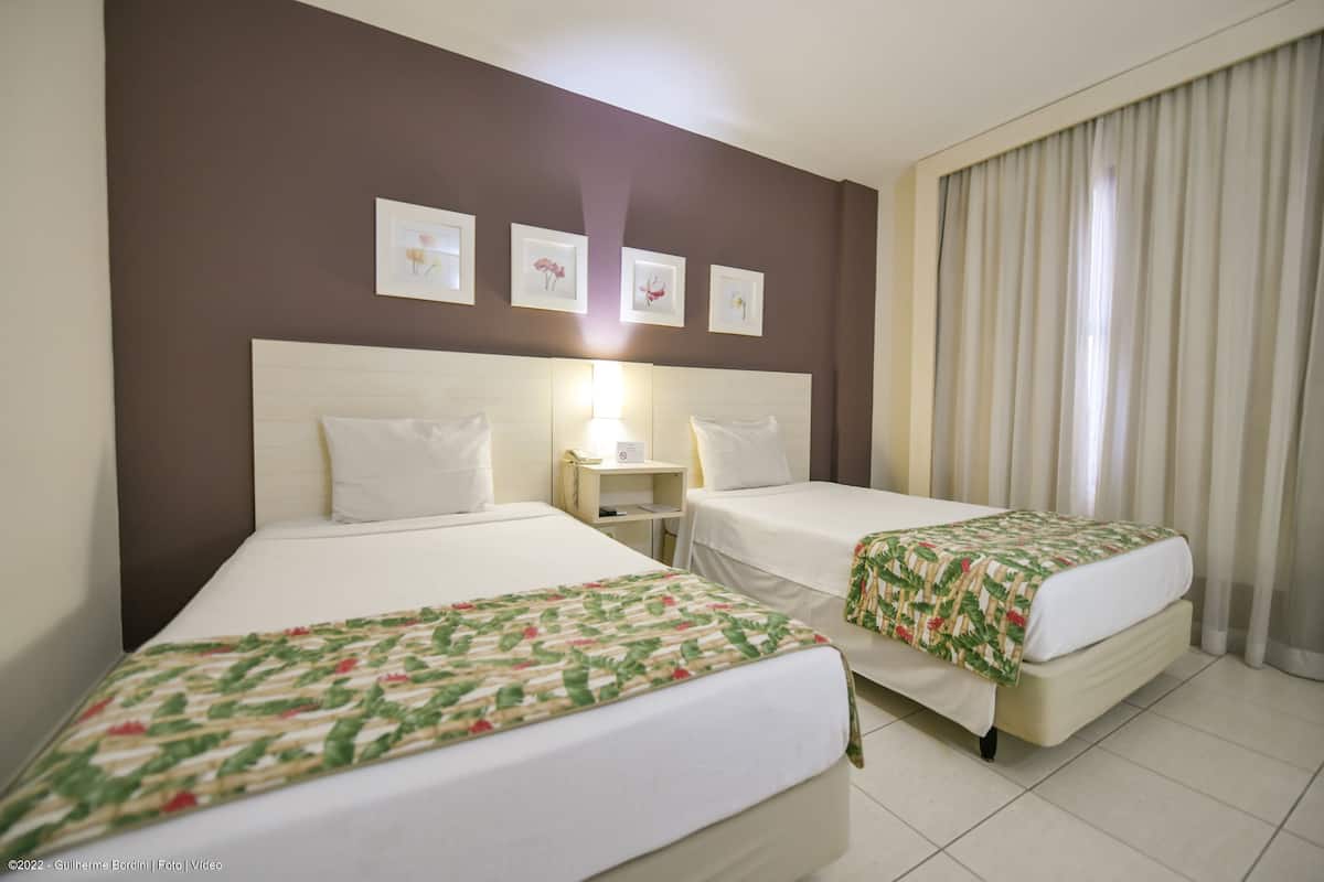 A hotel room with two beds, a nightstand, and a window with curtains.