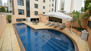A swimming pool with a sunbed area and a covered seating area.