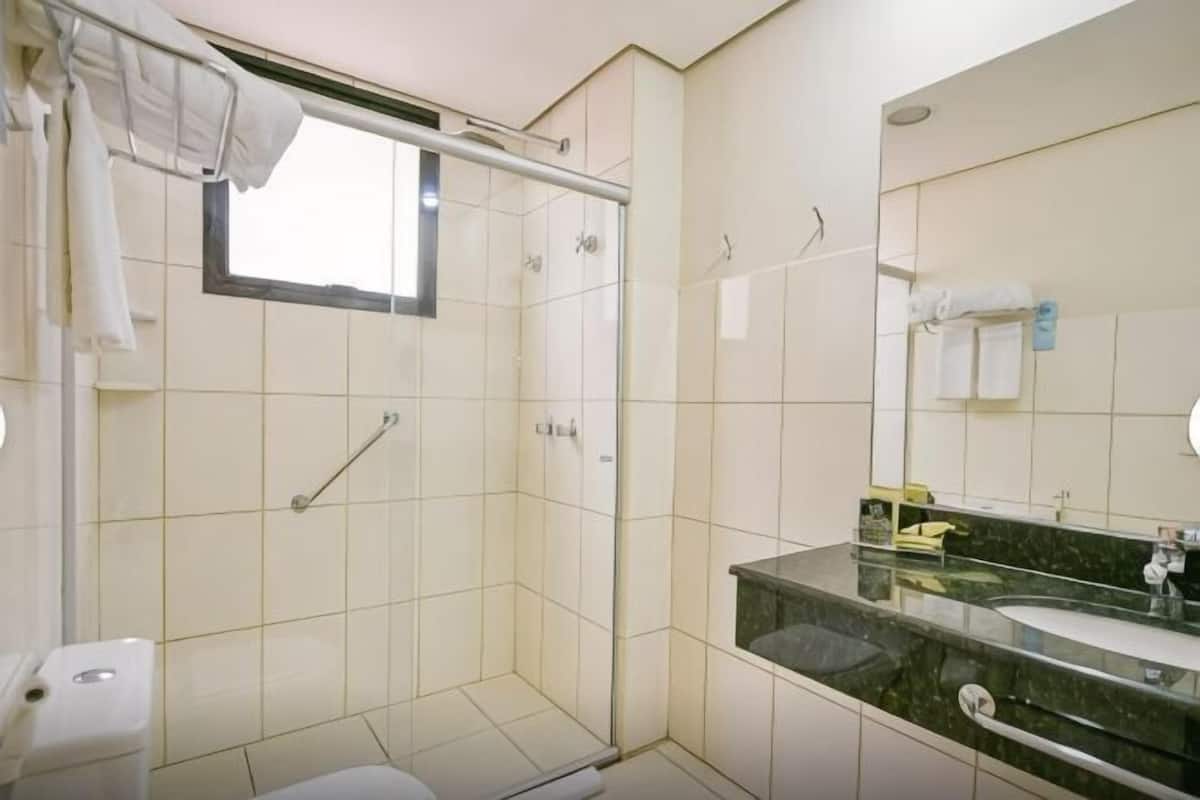 Un baño con ducha, inodoro, lavamanos y un espejo grande.
