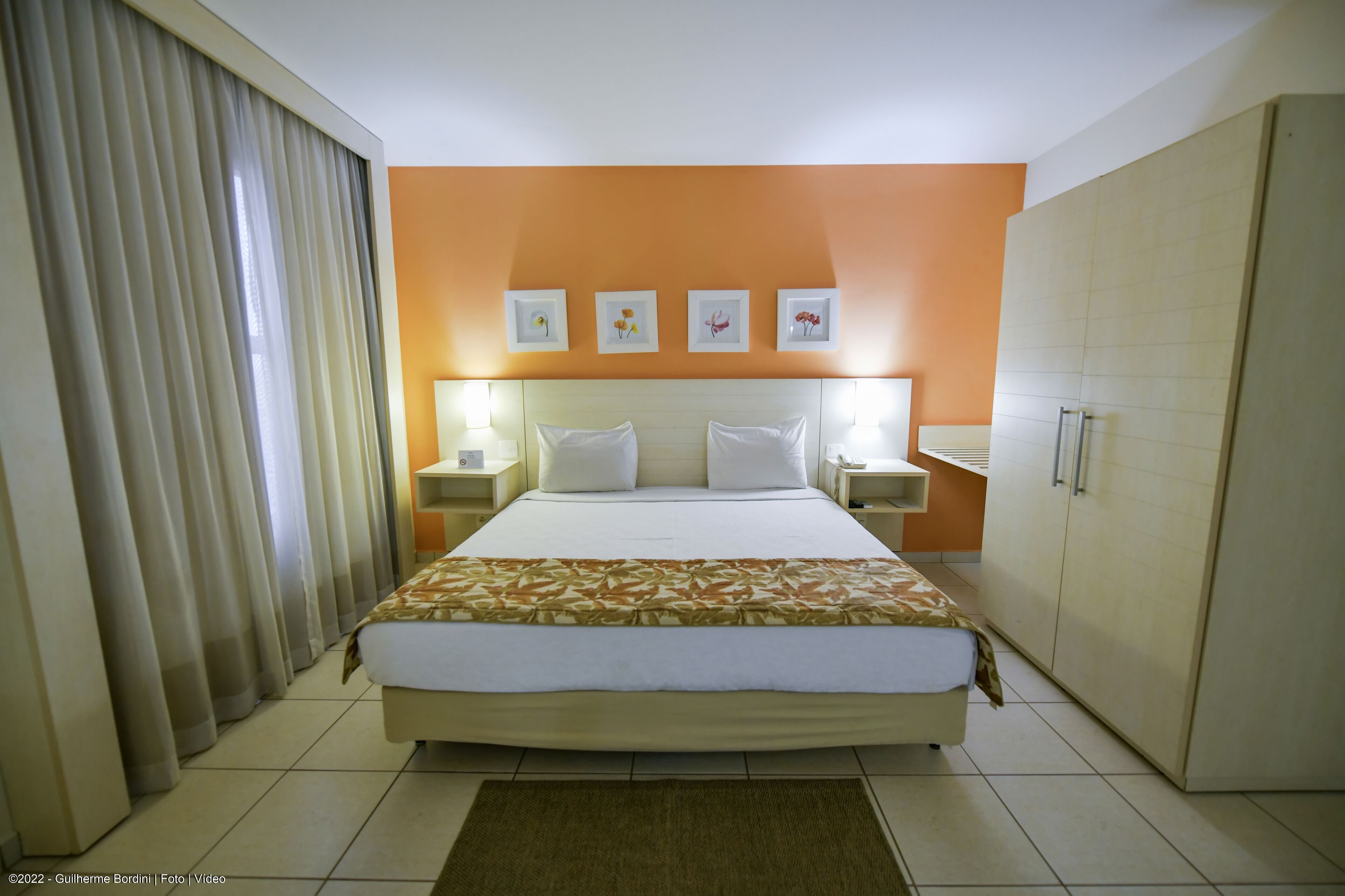 A hotel room with a large bed, two bedside tables, a wardrobe, and a curtain.