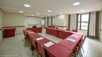 A conference room with a long table, chairs, a whiteboard, and a projector screen.