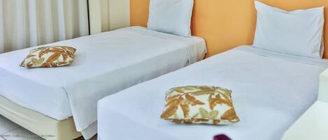 Dos camas individuales con sábanas y almohadas blancas a juego, un cuadro en la pared y una ventana con cortinas.