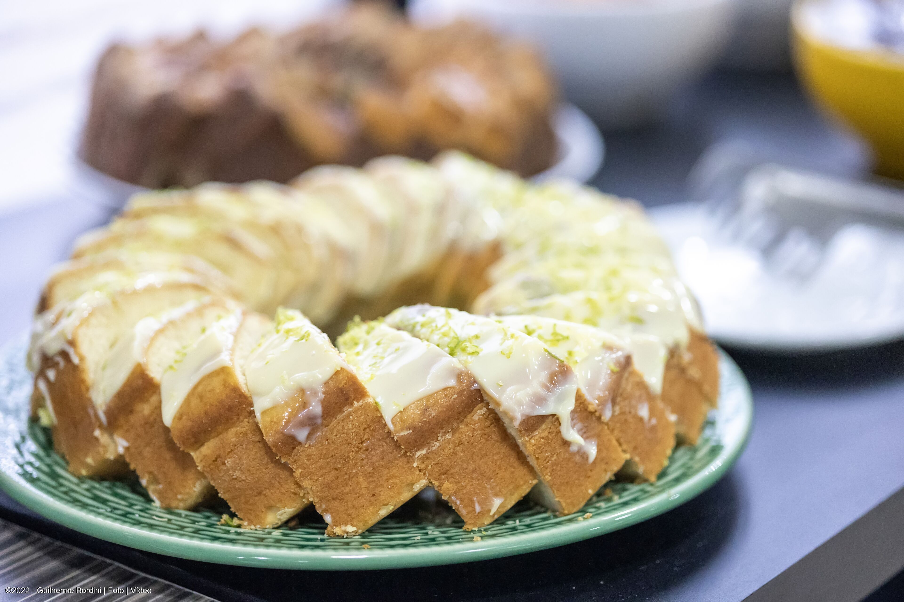 Um bolo bundt com cobertura branca sobre um prato verde.