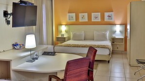 A hotel room with a bed, bedside tables, a desk with a lamp, a chair, and a TV mounted on the wall.